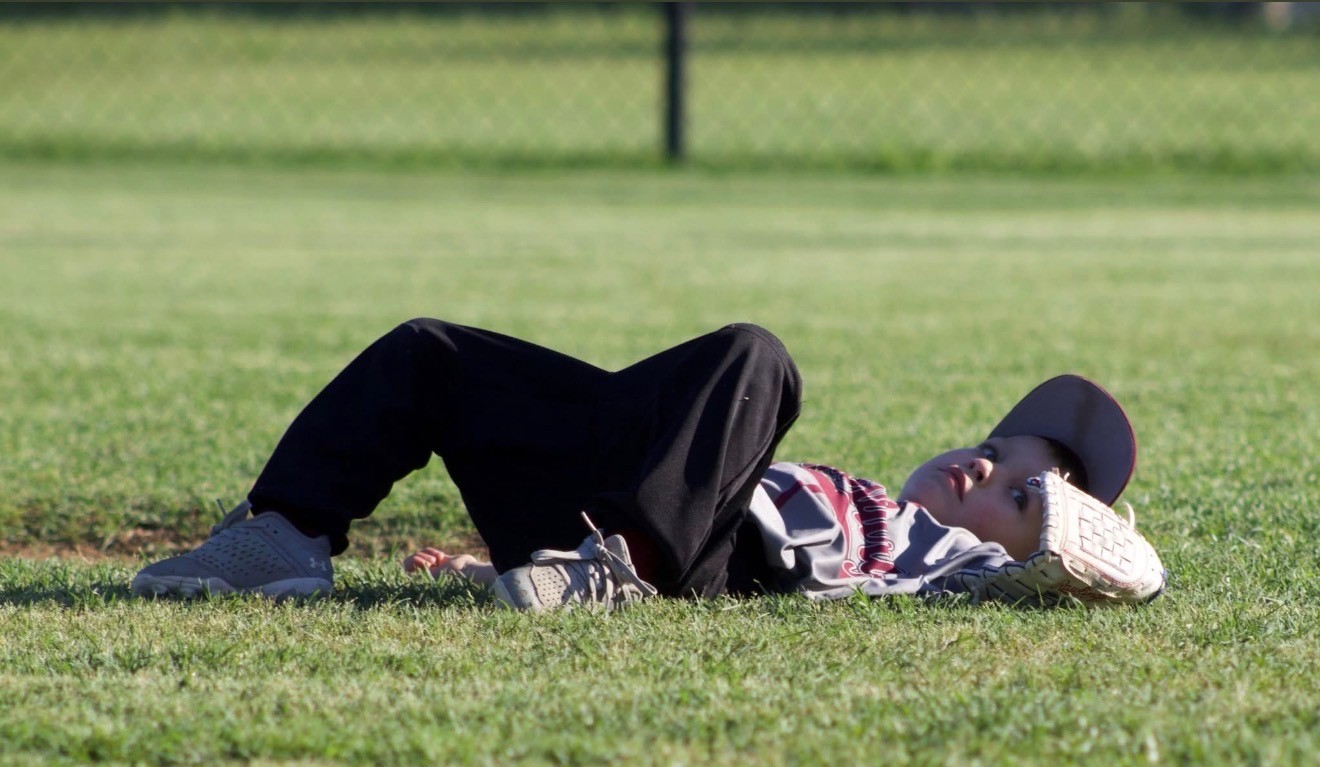 A young baseball player resting on the grass with a glove beneath their head.